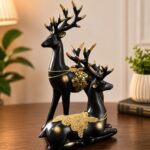 ELEGANT DESIGN: Set of 2 decorative reindeer figurines featuring a sophisticated black finish with luxurious golden accents and ornate floral embellishments, perfect for adding a touch of elegance to any space PREMIUM QUALITY: Crafted from high-quality resin material ensuring durability and long-lasting beauty, these Barahsingha deer sculptures showcase intricate detailing on the antlers and body PERFECT DIMENSIONS: Standing figurine measures 28 cm height x 16 cm length x 5 cm width, whilst the sitting figurine measures 19 cm height x 15 cm length x 4 cm width, ideal for tabletop display VERSATILE DECOR: Suitable for enhancing the aesthetic appeal of living rooms, office desks, mantels, shelves, or as a centrepiece for special occasions and festive celebrations READY TO DISPLAY: Comes as a complete pair with one standing and one sitting deer figurine, featuring detailed golden-tipped antlers and decorative chain accents for an opulent look